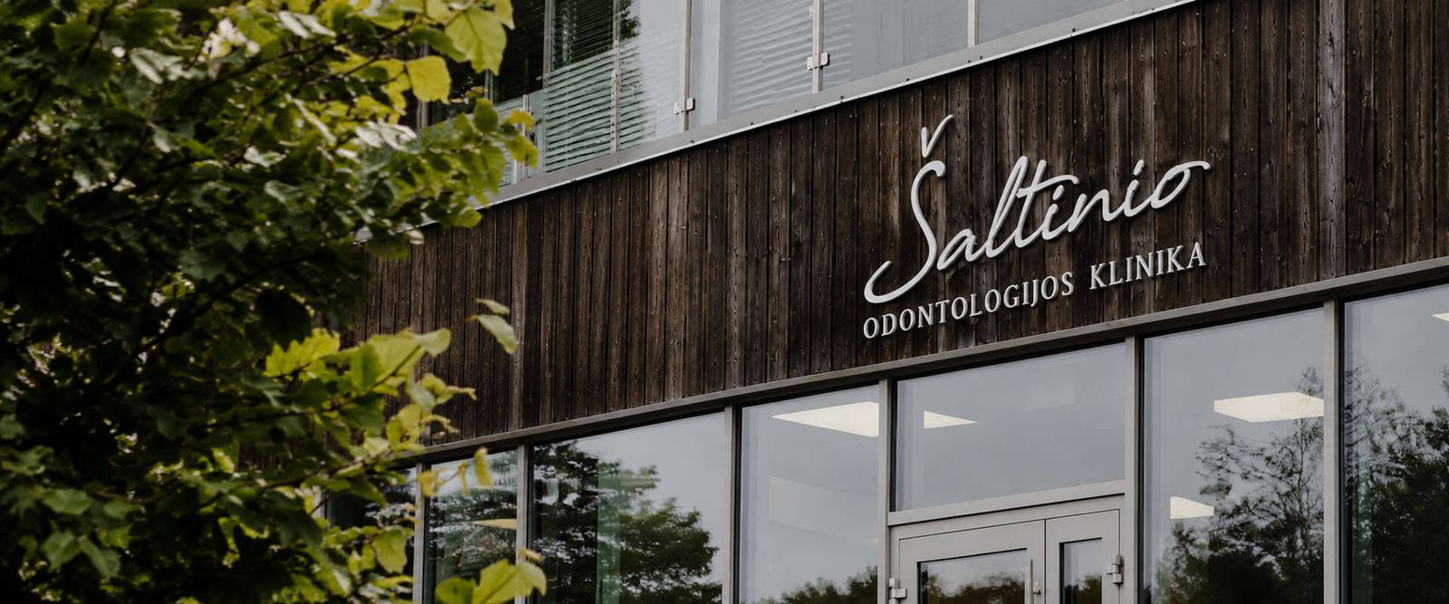 Šaltinio odontologijos klinikos pastatas Šaltinio gatvėje Raseiniuose: tamsi medinė fasado apdaila ir užrašas Šaltinio