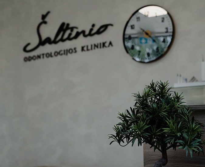 Klinikos interjeras: siena su Šaltinio logotipu, laikrodžiu ir bonsu